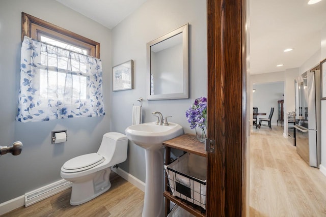 bathroom with toilet, a baseboard radiator, baseboards, and wood finished floors
