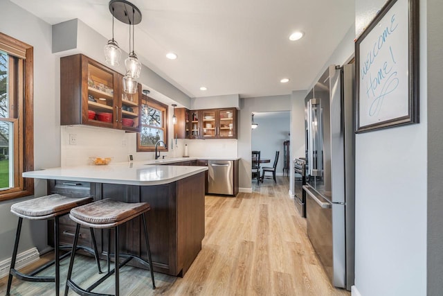 kitchen featuring glass insert cabinets, a peninsula, light wood-style floors, light countertops, and appliances with stainless steel finishes