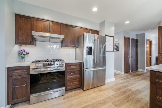 kitchen with tasteful backsplash, under cabinet range hood, light wood finished floors, light countertops, and appliances with stainless steel finishes