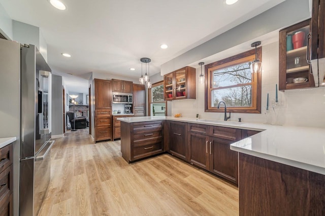 kitchen featuring stainless steel appliances, glass insert cabinets, a sink, a peninsula, and light countertops