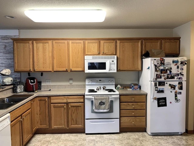 kitchen with light countertops, brown cabinets, a sink, and white appliances