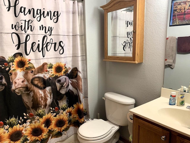 bathroom with toilet, curtained shower, vanity, and a textured wall