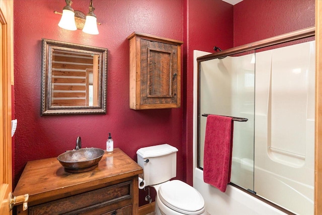 bathroom with toilet, shower / bath combination with glass door, vanity, and a textured wall