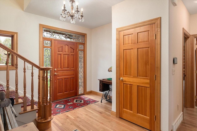 entrance foyer with an inviting chandelier, wood finished floors, visible vents, baseboards, and stairs