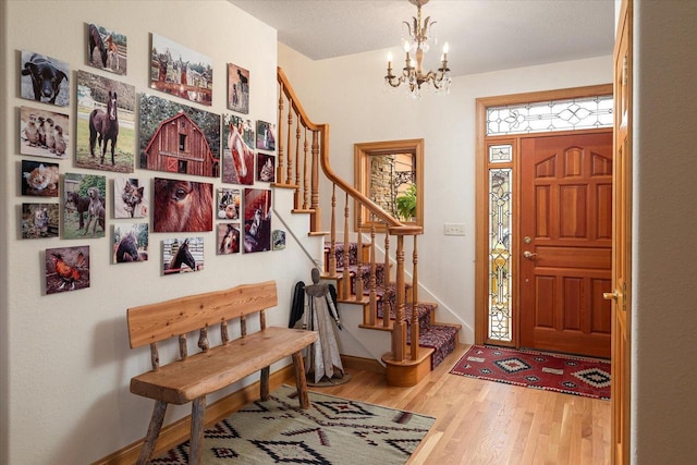 foyer entrance with baseboards, stairs, a notable chandelier, and wood finished floors