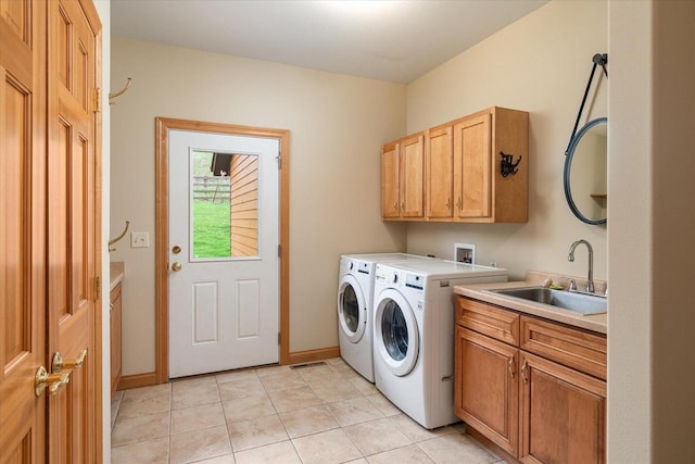 laundry area featuring a sink, cabinet space, light tile patterned flooring, washing machine and dryer, and baseboards