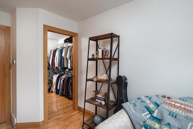 bedroom featuring a closet, baseboards, light wood-style flooring, and a walk in closet