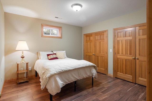 bedroom featuring dark wood finished floors, visible vents, baseboards, and two closets