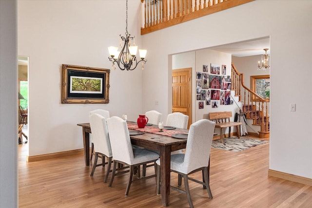 dining space featuring light wood-style flooring, baseboards, a towering ceiling, a chandelier, and stairs
