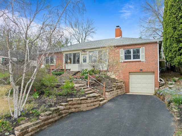 view of front of house featuring a chimney, brick siding, a garage, stairway, and aphalt driveway