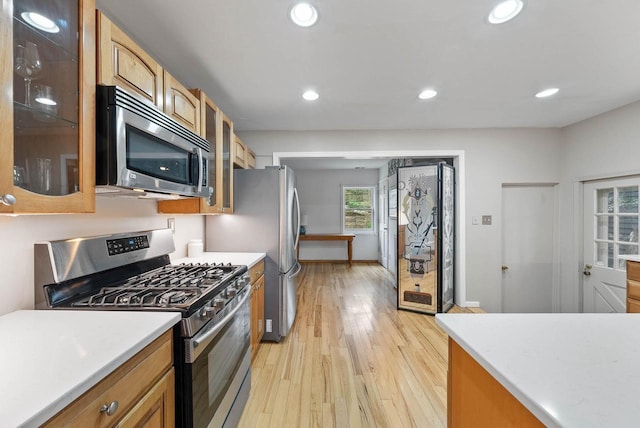 kitchen featuring appliances with stainless steel finishes, recessed lighting, glass insert cabinets, light countertops, and light wood-type flooring