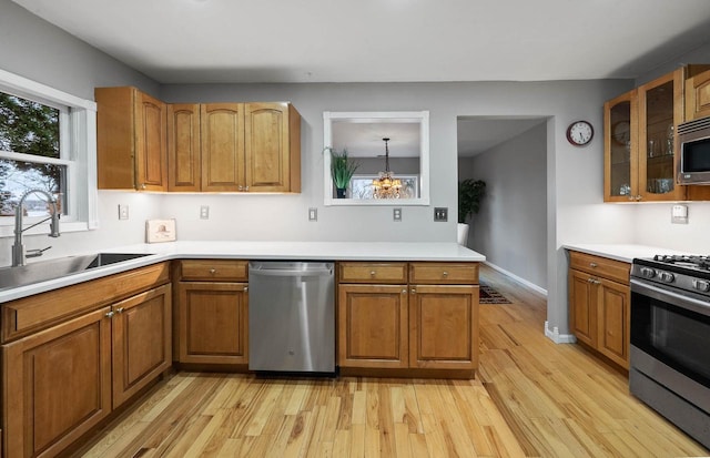 kitchen featuring light wood finished floors, glass insert cabinets, brown cabinets, a sink, and appliances with stainless steel finishes
