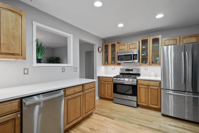 kitchen with light wood finished floors, glass insert cabinets, light countertops, appliances with stainless steel finishes, and recessed lighting