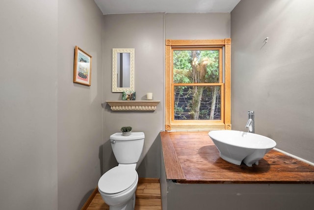 half bathroom with vanity, toilet, baseboards, and wood finished floors