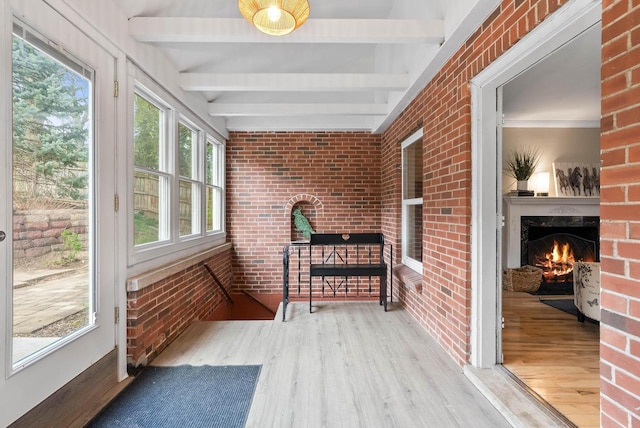 sunroom featuring a warm lit fireplace, brick wall, beam ceiling, and wood finished floors