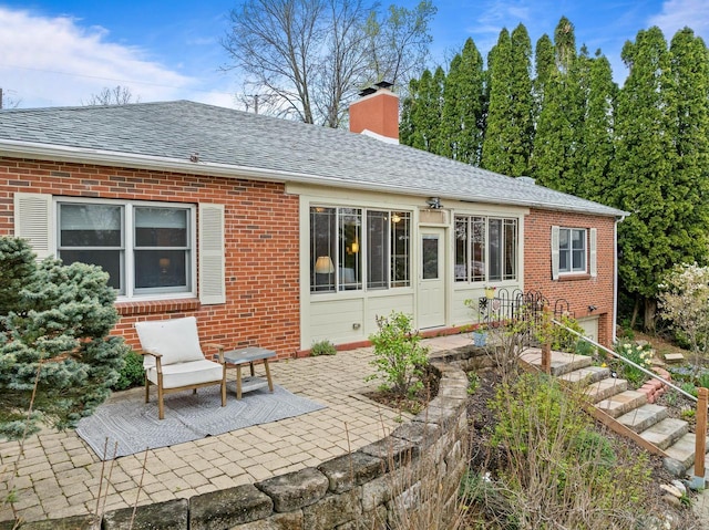 rear view of property with a patio area, a chimney, and brick siding
