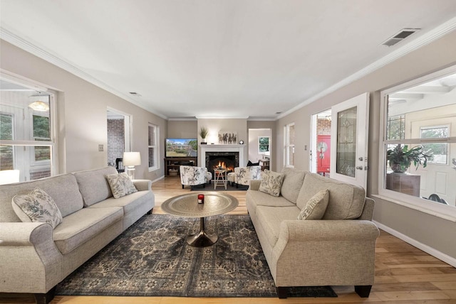 living area with a lit fireplace, a wealth of natural light, visible vents, and wood finished floors