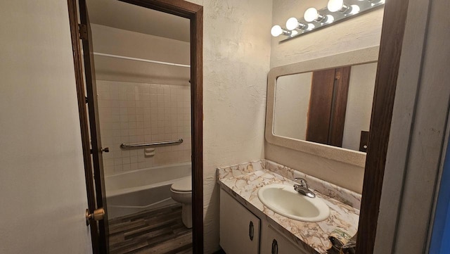 bathroom featuring toilet, shower / washtub combination, wood finished floors, vanity, and a textured wall