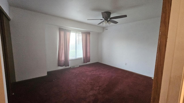 empty room with visible vents, a ceiling fan, and dark carpet