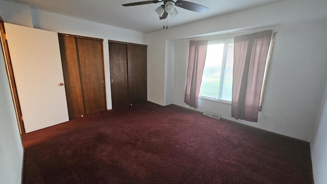 unfurnished bedroom featuring ceiling fan, dark colored carpet, visible vents, and two closets