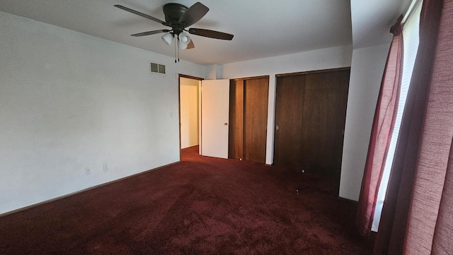 unfurnished bedroom featuring multiple closets, carpet floors, a ceiling fan, and visible vents