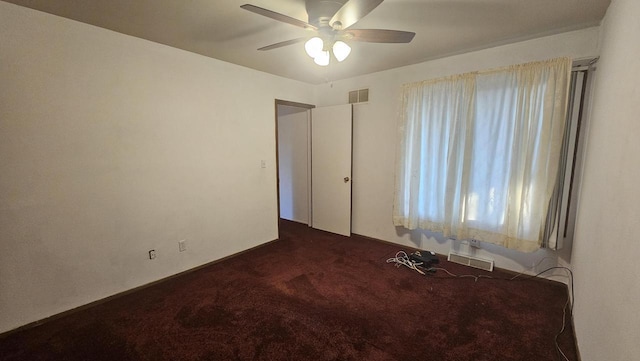 empty room with visible vents, dark colored carpet, and ceiling fan