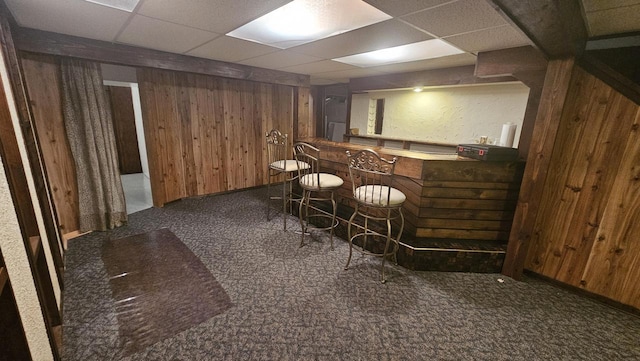 bar with baseboards, wooden walls, a bar, and carpet floors