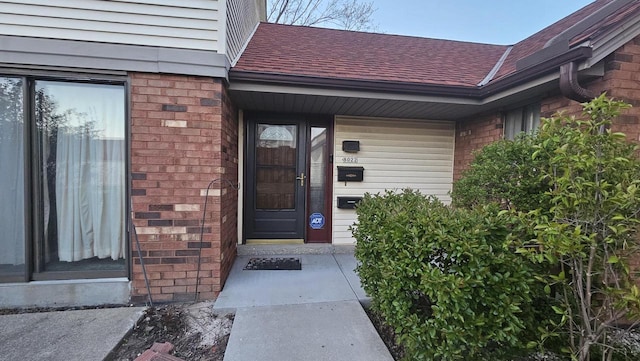 entrance to property with brick siding and roof with shingles