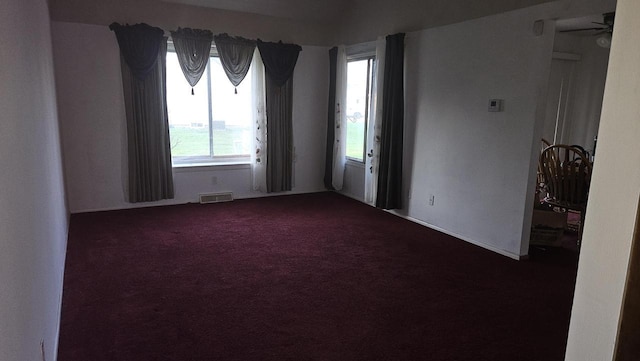 spare room featuring a healthy amount of sunlight, dark colored carpet, and visible vents