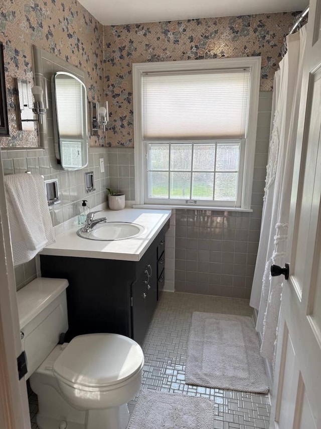 1651 E Ridge Rd, Beloit, WI 53511 - bathroom featuring tile walls, toilet, vanity, wallpapered walls, and a wainscoted wall
