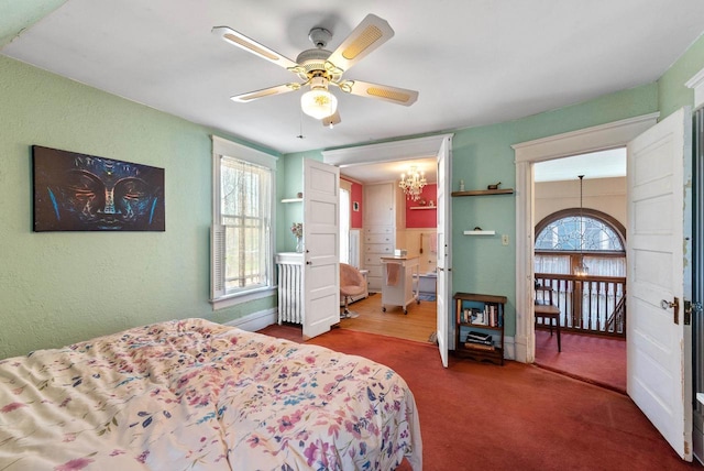 carpeted bedroom featuring ceiling fan with notable chandelier and a textured wall