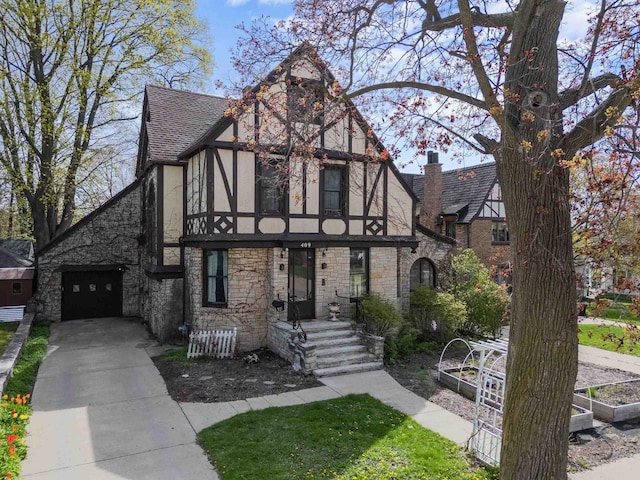 english style home with a shingled roof, stucco siding, stone siding, and driveway
