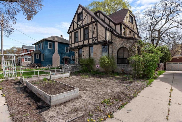 english style home featuring stone siding, stucco siding, and a vegetable garden
