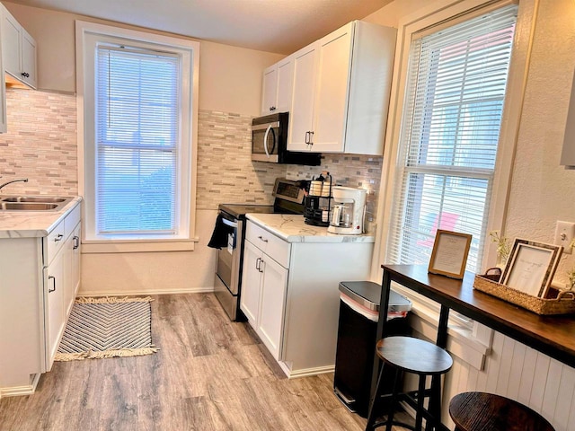 201 S Beaumont Rd, Prairie Du Chien, WI 53821 - kitchen with light wood-style flooring, a sink, white cabinetry, appliances with stainless steel finishes, and decorative backsplash