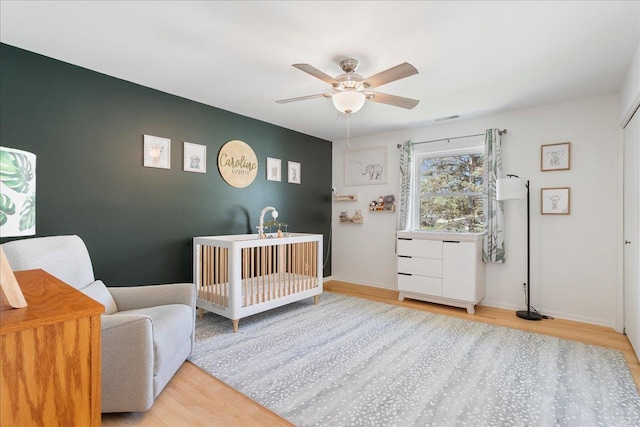 bedroom featuring a ceiling fan, light wood-style flooring, baseboards, a nursery area, and visible vents