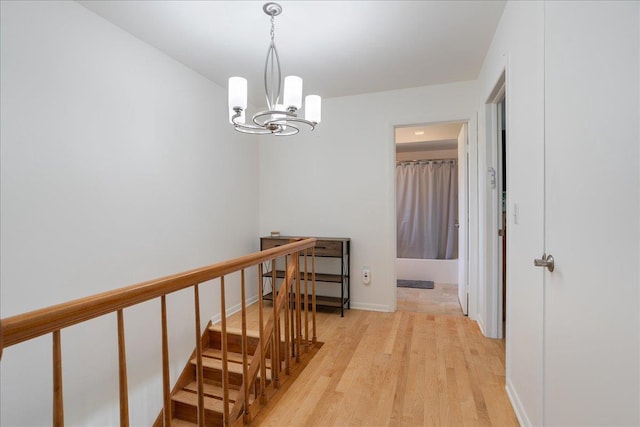 hall with light wood finished floors, an upstairs landing, and a notable chandelier