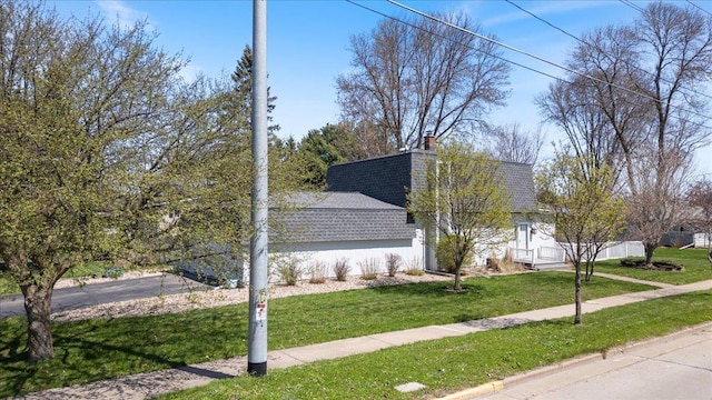 view of side of property with roof with shingles, a chimney, and a lawn