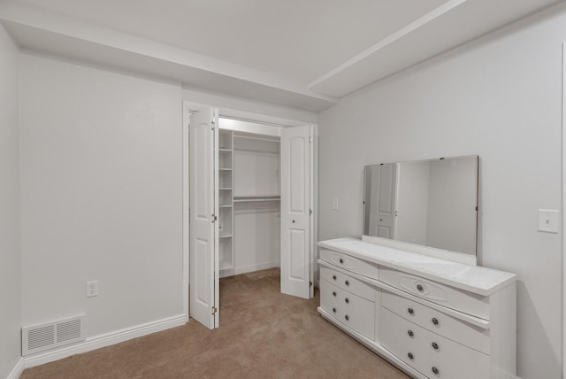 unfurnished bedroom with a closet, light colored carpet, visible vents, a walk in closet, and baseboards