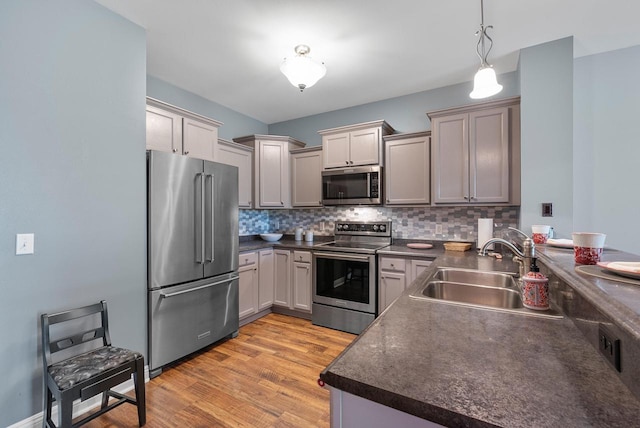 kitchen with a sink, stainless steel appliances, tasteful backsplash, dark countertops, and light wood-style floors