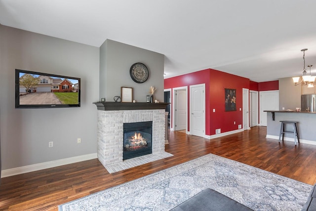 living room with a fireplace, a chandelier, baseboards, and wood finished floors