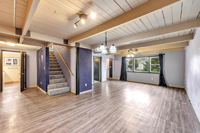 unfurnished living room with wood finished floors, baseboards, beam ceiling, and stairs