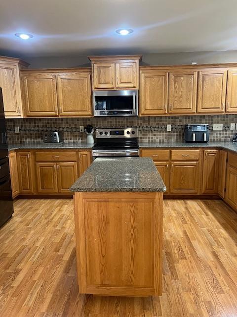 1075 Grant St, Fennimore, WI 53809 - kitchen with stainless steel appliances, light wood-style flooring, dark stone countertops, backsplash, and a center island