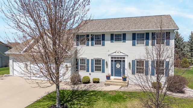 colonial house featuring entry steps, a shingled roof, concrete driveway, and a front yard