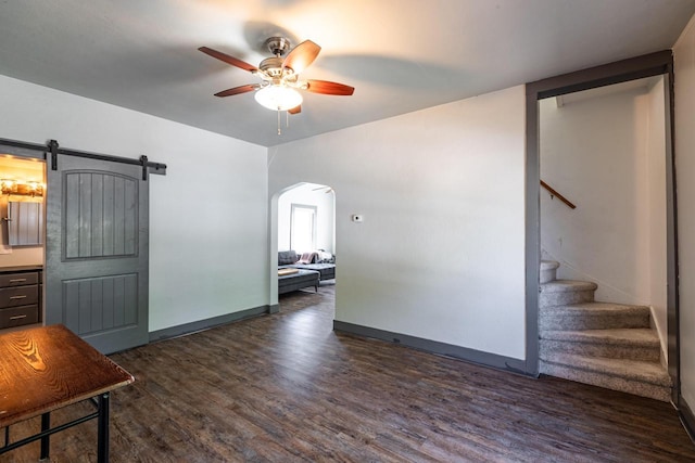 unfurnished living room with a ceiling fan, a barn door, arched walkways, stairway, and dark wood-style floors