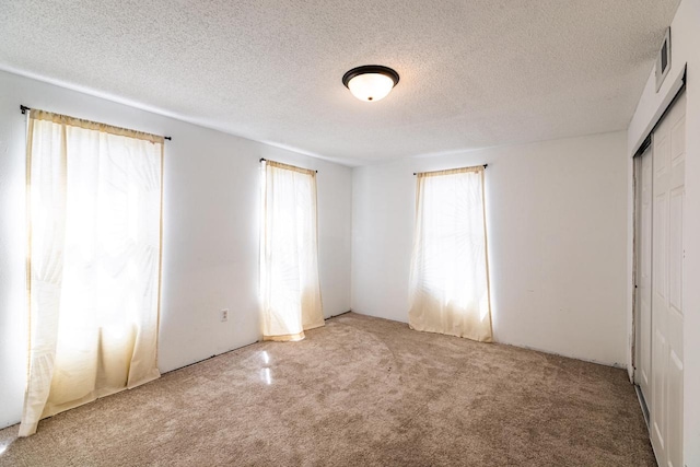 unfurnished bedroom featuring light carpet, a textured ceiling, a closet, and visible vents