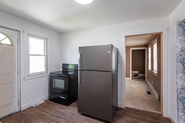 kitchen with freestanding refrigerator, black / electric stove, dark wood finished floors, visible vents, and baseboards
