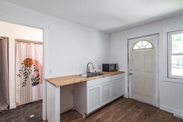 interior space with stainless steel microwave, a sink, wood counters, visible vents, and dark wood-style floors