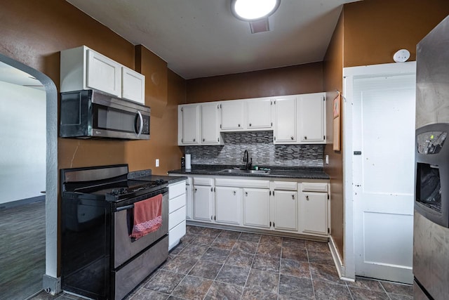 kitchen with a sink, dark countertops, stainless steel appliances, white cabinets, and tasteful backsplash