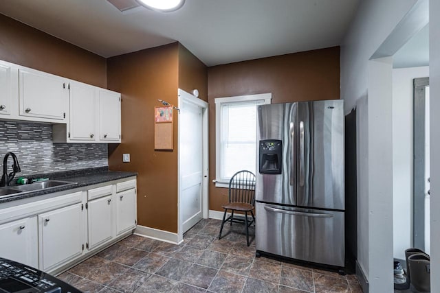 kitchen with baseboards, a sink, stainless steel fridge, dark countertops, and tasteful backsplash