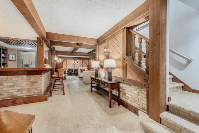 living area featuring carpet floors, stairs, wood walls, and beam ceiling